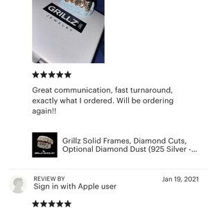 Puede incluir: Primer plano de una parrilla de oro con detalles de diamantes. La parrilla se muestra en una caja blanca con el texto "Grillz Jewelry" impreso en ella.