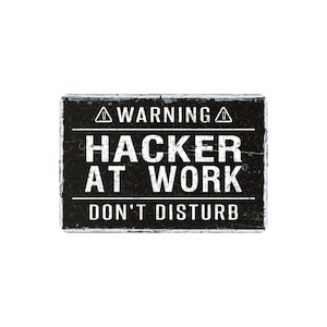 May include: A rectangular black sign with white text that reads "WARNING HACKER AT WORK DON'T DISTURB". The sign has a distressed, weathered appearance, with a white border.