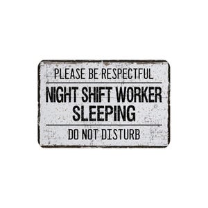 May include: Rectangular white sign with black text that reads "PLEASE BE RESPECTFUL NIGHT SHIFT WORKER SLEEPING DO NOT DISTURB". The sign has a distressed, vintage look.