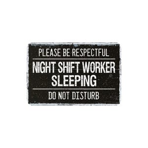 May include: A rectangular black sign with white text that reads "PLEASE BE RESPECTFUL NIGHT SHIFT WORKER SLEEPING DO NOT DISTURB". The sign has a distressed, vintage appearance.