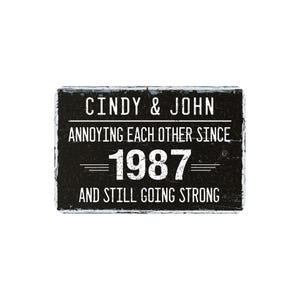 May include: A rectangular black sign with white text that reads "Cindy & John Annoying Each Other Since 1987 And Still Going Strong." The sign has a distressed, rustic appearance.