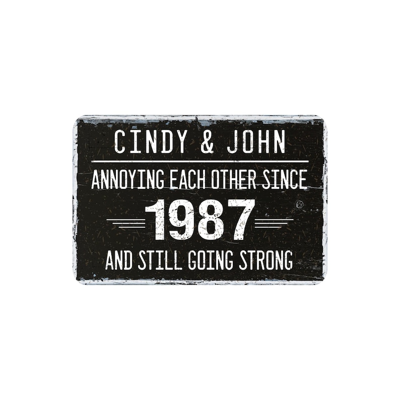 May include: A rectangular black sign with white text that reads "Cindy & John Annoying Each Other Since 1987 And Still Going Strong." The sign has a distressed, rustic appearance.