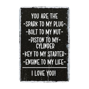May include: A rectangular black metal sign with white text. The text reads: "YOU ARE THE -SPARK TO MY PLUG- -BOLT TO MY NUT- -PISTON TO MY- CYLINDER -KEY TO MY STARTER- -ENGINE TO MY LIFE- I LOVE YOU!"