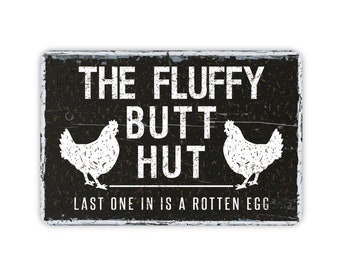 May include: Black and white sign with distressed woodgrain texture. The sign reads "The Fluffy Butt Hut" with a chicken silhouette on each side. The bottom of the sign reads "Last one in is a rotten egg."