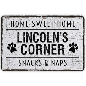 May include: A rectangular, distressed white sign with black text that reads "HOME SWEET HOME" above "LINCOLN'S CORNER" and "SNACKS & NAPS". Black paw prints flank "LINCOLN'S CORNER". The sign has a rustic, weathered appearance.