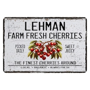 May include: A white sign with black text that reads "LEHMAN FARM FRESH CHERRIES". The sign also has the text "PICKED DAILY", "SWEET JUICY", "THE FINEST CHERRIES AROUND", and "LOCAL ORGANIC ALWAYS FRESH". A vintage illustration of a cherry branch with red cherries is in the center of the sign.