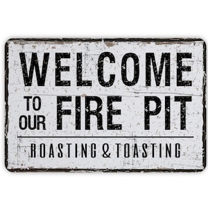 May include: A rectangular, distressed white sign with black text that reads "WELCOME TO OUR FIRE PIT ROASTING & TOASTING." The sign has a rustic, weathered appearance, suggesting outdoor use. The text is in a bold, sans-serif font.