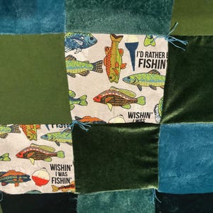 May include: A patchwork quilt with a fishing theme. The quilt features squares of teal, green, and patterned fabric with fish illustrations and the text "I'd Rather Be Fishin'" and "Wishin' I Was Fishin'".