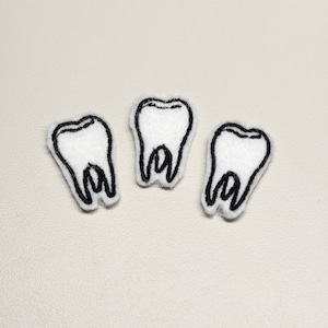 May include: Three white felt teeth with black outlines. The teeth are arranged in a row.