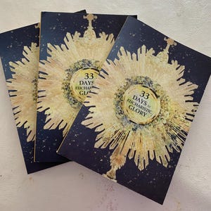 Pode incluir: Três livretos azul marinho com um desenho de explosão solar dourado e branco. O centro do desenho tem o texto "33 Days to Eucharistic Glory". Os livretos estão empilhados uns sobre os outros.
