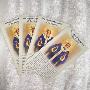 May include: A white ceramic mug with a black handle and the text "But First, Coffee" in a black, bold font. The mug is on a white surface. The mug is approximately 10 cm tall.