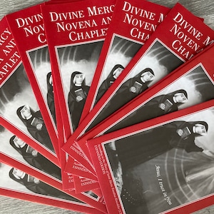May include: A stack of red pamphlets with the title "Divine Mercy Novena and Chaplet" printed on the front. The pamphlets feature a black and white image of a nun holding a book. The text "Jesus, I trust in You" is printed on the bottom of the pamphlet.