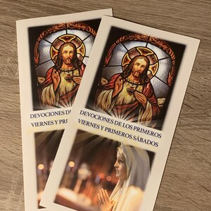 May include: Two religious prayer cards. Each card features an image of Jesus with a heart and a stained-glass window background. The text "DEVOCIONES DE LOS PRIMEROS VIERNES Y PRIMEROS SÁBADOS" is printed on the cards.