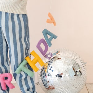 Puede incluir: Un ni&ntilde;o sostiene una pancarta de cumplea&ntilde;os de fieltro con una bola de discoteca en el fondo. La pancarta est&aacute; hecha de letras de fieltro de colores que deletrean "cumplea&ntilde;os".