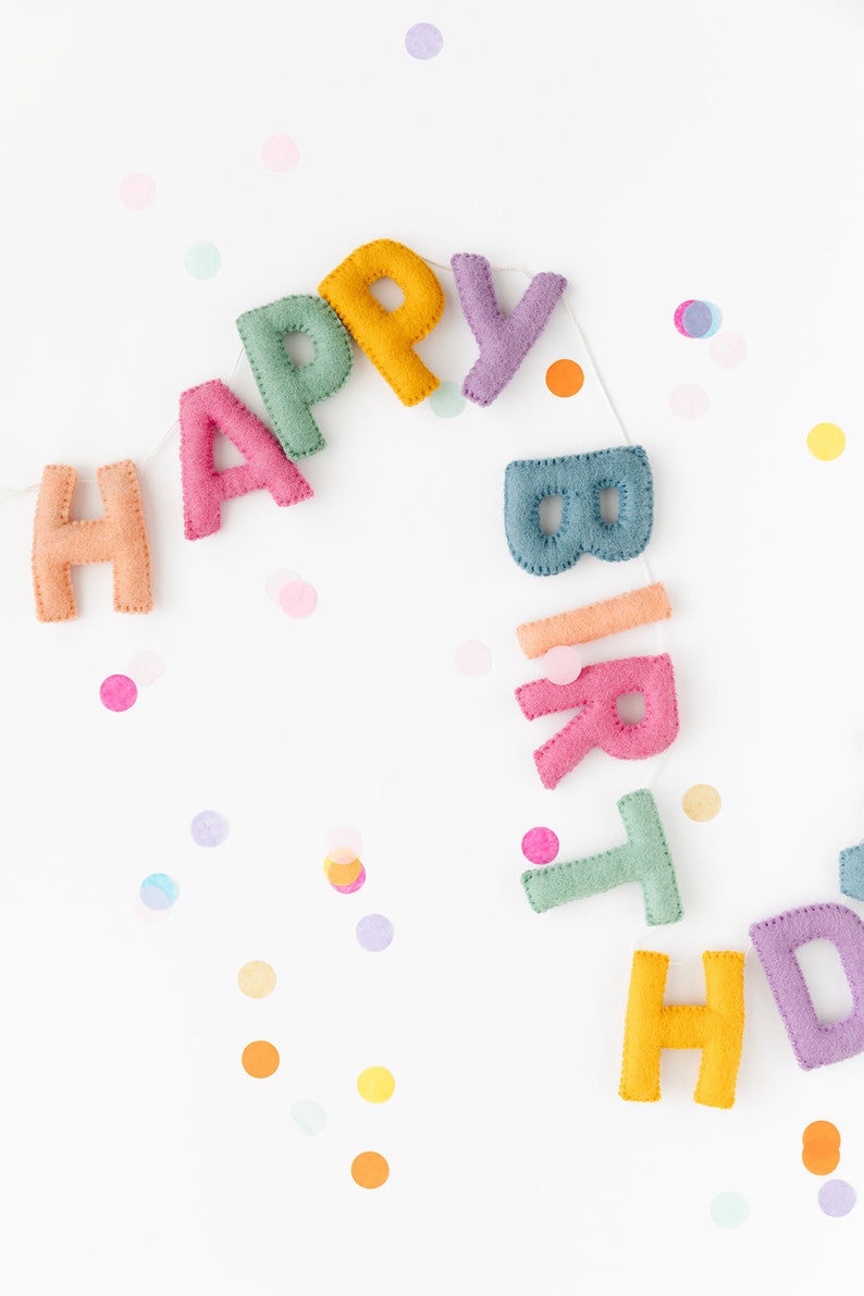 Puede incluir: Una pancarta de fieltro de colores que deletrea "Happy Birthday" con confeti esparcidos a su alrededor.