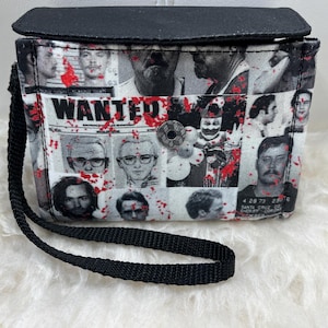 May include: A rectangular wristlet bag featuring a black fabric flap and a black wrist strap. The body of the bag displays a collage of black and white mugshot-style portraits overlaid with red splatters and the word WANTED in bold black letters.
