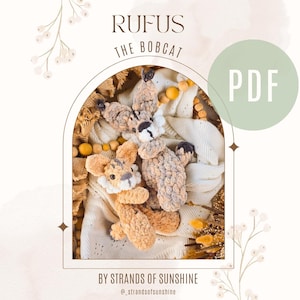 May include: A crochet bobcat toy named Rufus, with tan and cream colors, is displayed in a decorative setting. The image includes the text "RUFUS THE BOBCAT" and "PDF". The design is by Strands of Sunshine.