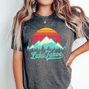 May include: A dark grey t-shirt with a vintage-style graphic of mountains and a sunset with the text "Lake Tahoe" in a turquoise blue font.