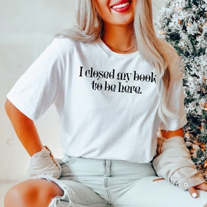 May include: A white t-shirt with the text "I closed my book to be here." printed in black.