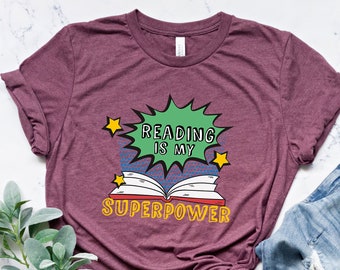 May include: A maroon t-shirt with a graphic of a book and the text "Reading is my superpower" in a comic book style.