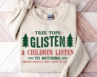 May include: A cream-colored sweatshirt with the text "TREE TOPS GLISTEN & CHILDREN LISTEN TO NOTHING." The text is in green and red, with a distressed font. Two green Christmas trees flank the word "GLISTEN".