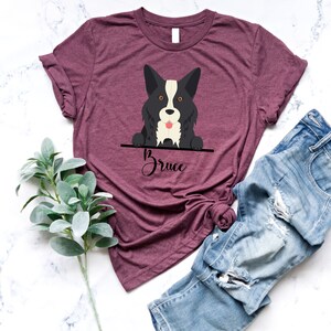 Peut inclure: Un t-shirt marron avec un chien de dessin anim&eacute; noir et blanc qui regarde par-dessus le haut. Le chien a une bande blanche sur le visage et le texte "Bruce" est &eacute;crit sous le chien.