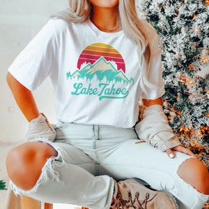 May include: White t-shirt with a retro sunset graphic featuring mountains and the text "Lake Tahoe" in teal.