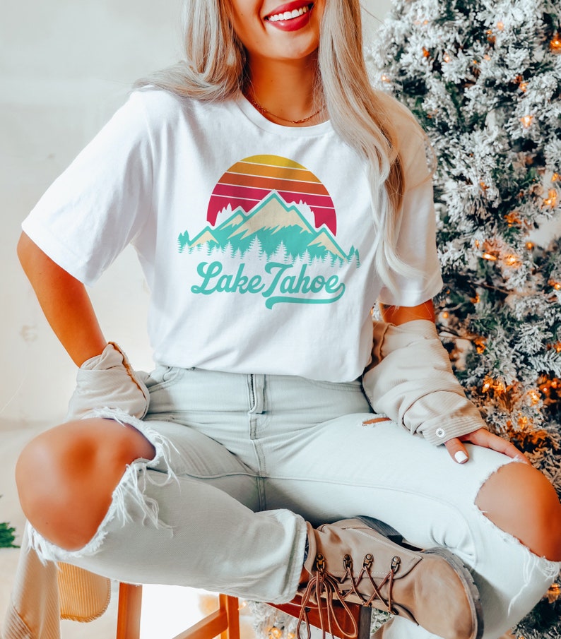 May include: White t-shirt with a retro sunset graphic featuring mountains and the text "Lake Tahoe" in teal.
