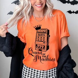 May include: Orange t-shirt with a black graphic of a slot machine with the text "Jackpot Slots 777" and "Queen of the Machine".