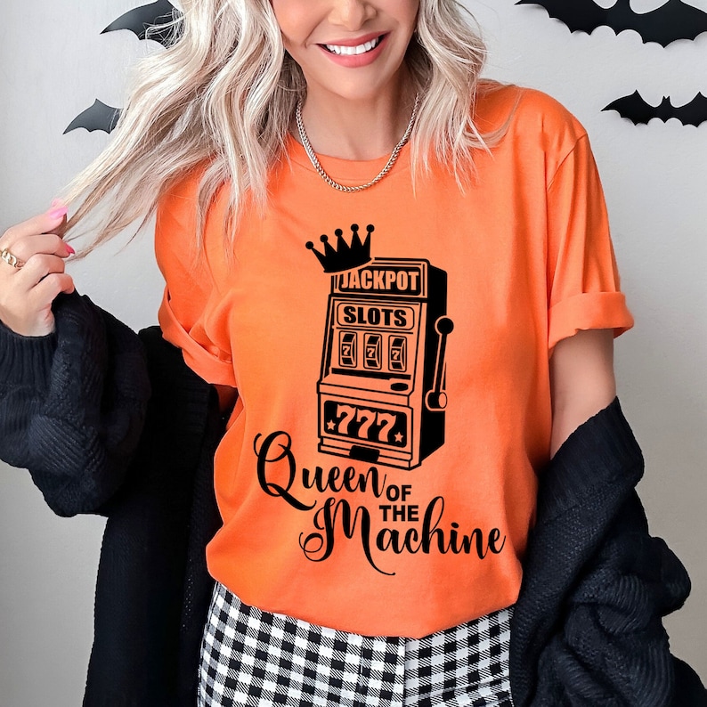 May include: Orange t-shirt with a black graphic of a slot machine with the text "Jackpot Slots 777" and "Queen of the Machine".