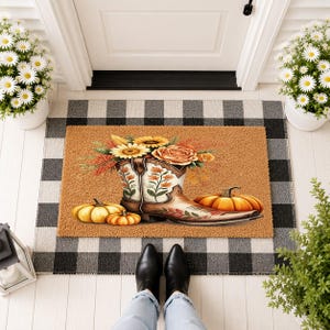May include: A rectangular tan coir doormat featuring a central illustration of a white cowboy boot filled with orange roses and yellow sunflowers, flanked by two orange pumpkins, resting on a black and white buffalo check floor mat.