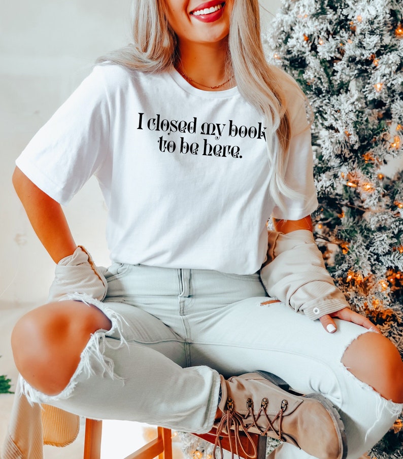 May include: A white t-shirt with the text "I closed my book to be here." printed in black.