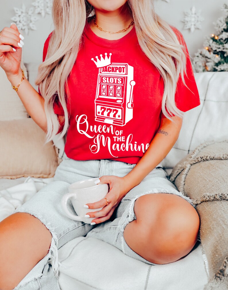 May include: A red t-shirt with a white graphic of a slot machine with the text "Jackpot Slots" and "Queen of the Machine".