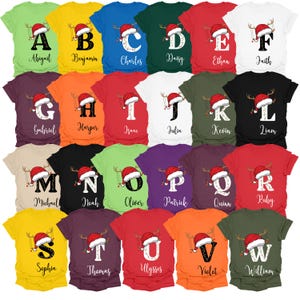 May include: A collection of colorful t-shirts, each featuring a letter of the alphabet and a name, along with a Christmas-themed design. The shirts are in various colors, including green, yellow, and red.