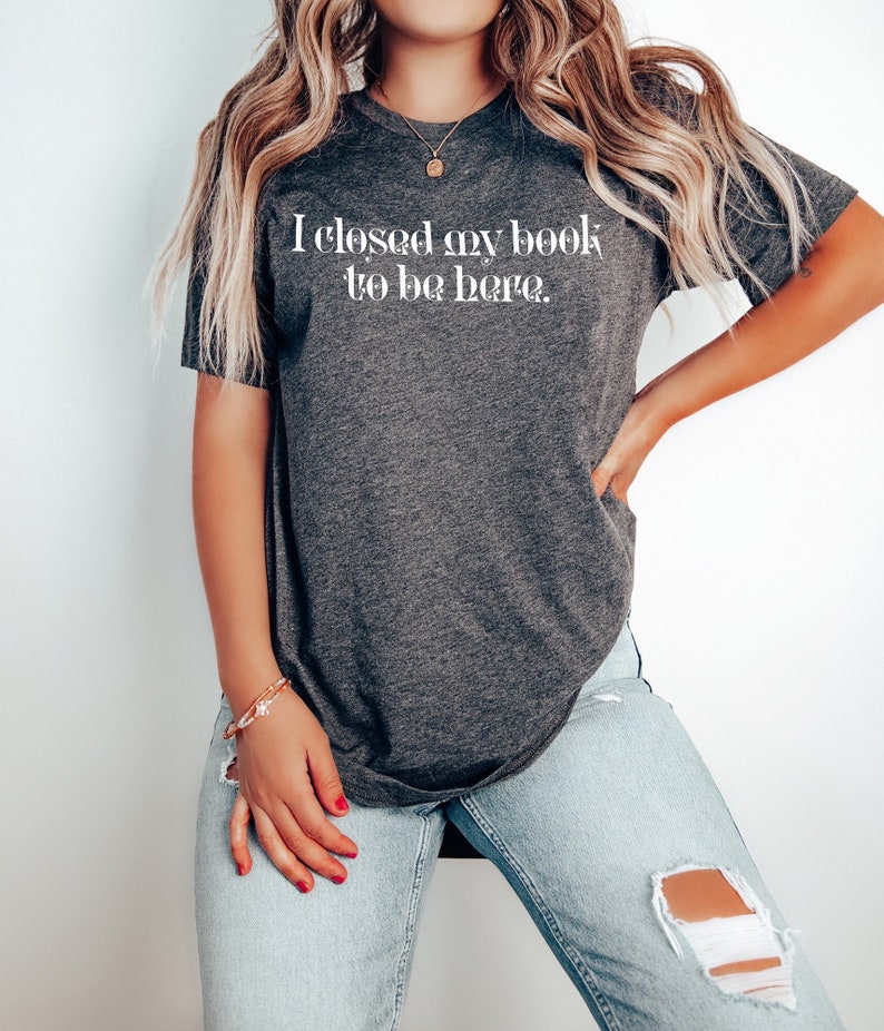 May include: A dark grey t-shirt with the text "I closed my book to be here." printed in white.