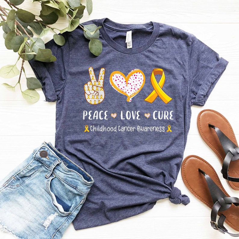 May include: A navy blue t-shirt with a peace sign, heart, and yellow ribbon. The text "Peace Love Cure" and "Childhood Cancer Awareness" is printed on the shirt.