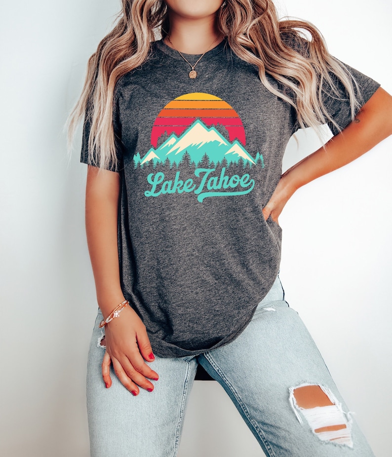 May include: A dark grey t-shirt with a vintage-style graphic of mountains and a sunset with the text "Lake Tahoe" in a turquoise blue font.