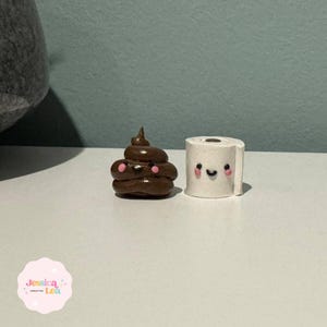 May include: A brown, smiling poop emoji and a white toilet paper roll with a smiling face. Both are small, handmade figurines. The poop emoji has pink cheeks and the toilet paper roll has a black smile and pink cheeks.