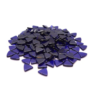 Op de afbeelding: Een stapel kleine, donkerblauwe driehoekige glazen mozaïektegels.