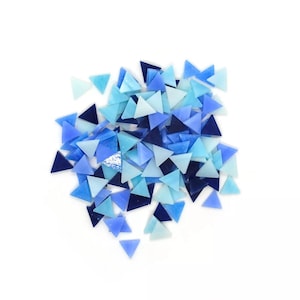Op de afbeelding: Een stapel blauwe en lichtblauwe glazen driehoekige mozaïektegels. De tegels zijn in verschillende tinten blauw en lichtblauw.