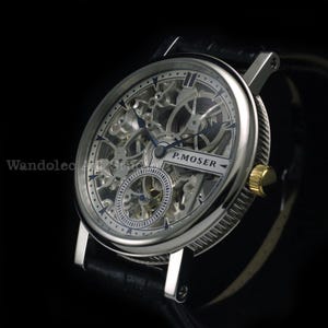 May include: A silver skeleton watch with a black leather band. The watch face features intricate gears and the text "P.MOSER". The watch has a gold-colored crown and a round face.