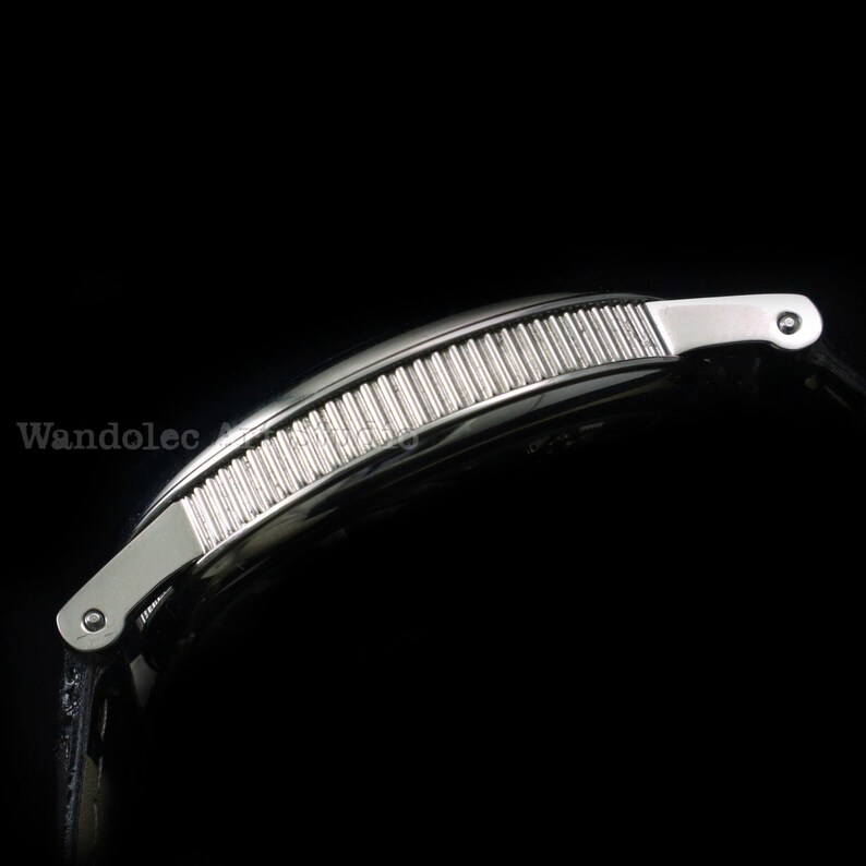 May include: A silver-toned watch with a black band. The watch face is curved and features a series of vertical, parallel lines. The band appears to be leather. The watch is set against a black background.