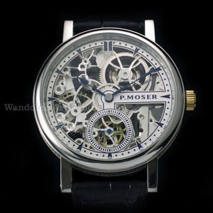 May include: A silver-toned skeleton watch with a black leather band. The watch face reveals intricate internal mechanisms, with blue hands and accents. The watch has a gold-colored crown and the brand name "P. MOSER" is visible.