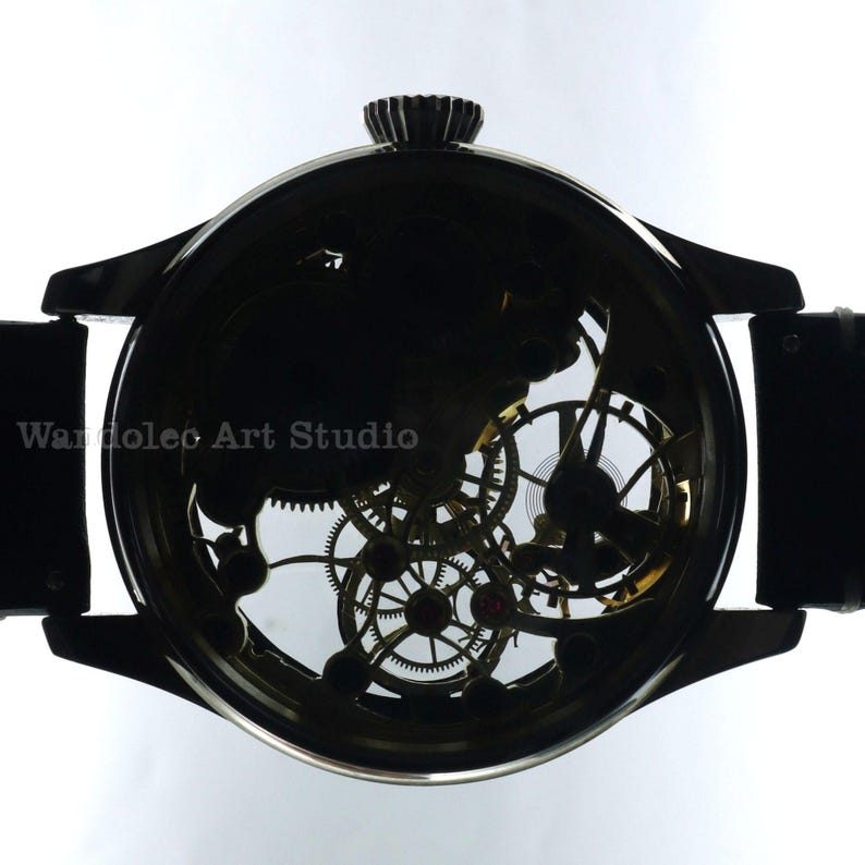 May include: A black wristwatch with a transparent face, showcasing the intricate inner workings of the watch's gears and mechanisms. The watch has a black leather band and a crown at the top. The text "Wandolec Art Studio" is visible.
