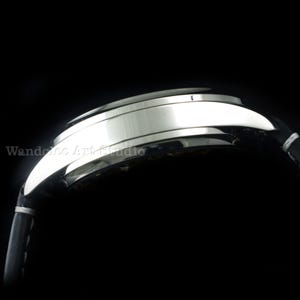 May include: Close-up of a silver wristwatch with a black leather band. The watch face is not visible. The band is stitched with white thread. The watch is set against a black background. The text "Wandelco Art Studio" is visible.
