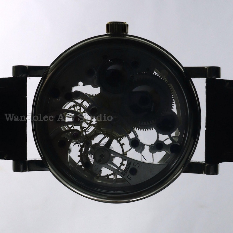 May include: A black skeleton watch with visible gears and a leather strap. The watch face displays intricate mechanical components. The text "Wanolec Art Studio" is visible on the watch face.