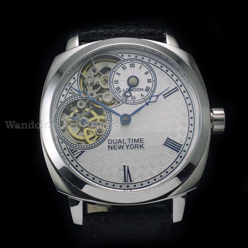 Puede incluir: Reloj de pulsera plateado con esfera texturizada y agujas azules. El reloj presenta dos esferas m&aacute;s peque&ntilde;as y el texto "DUAL TIME NEW YORK". Tiene una correa de cuero negro.