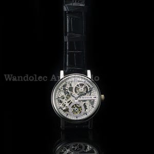 May include: A silver-toned skeleton watch with a black leather band. The watch face reveals intricate internal mechanisms, with the brand name "P. MOSER" visible. The watch is set against a black background, with a reflection below.