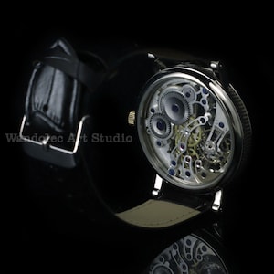 May include: A close-up of a mechanical wristwatch with a black leather band. The watch face is transparent, revealing the intricate internal gears and mechanisms. The watch has a silver-colored case and a gold-colored crown.