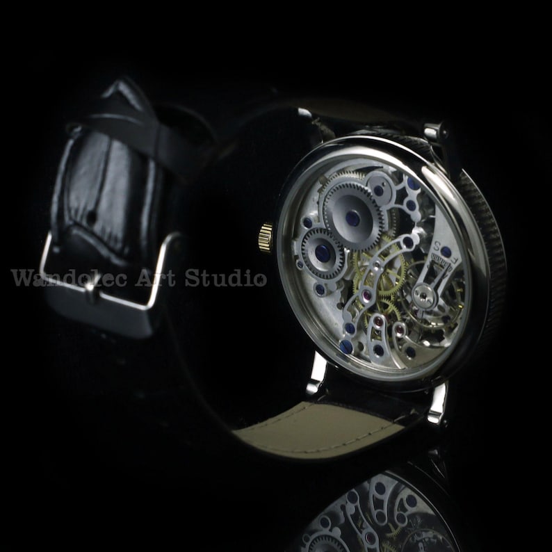 May include: A close-up of a mechanical wristwatch with a black leather band. The watch face is transparent, revealing the intricate internal gears and mechanisms. The watch has a silver-colored case and a gold-colored crown.